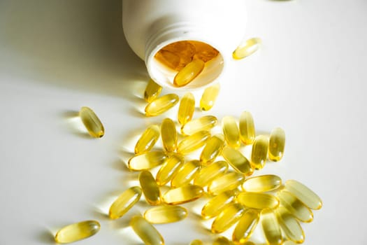 Pile of yellow softgel capsules Omega 3 fish oil scuttered from a white bottle bottle. Cod liver, fish oil. Filled soft gel supplements for diet. Health care concept