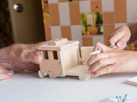 A five-year-old boy independently assembles a wooden construction kit with a screwdriver. Hands close-up