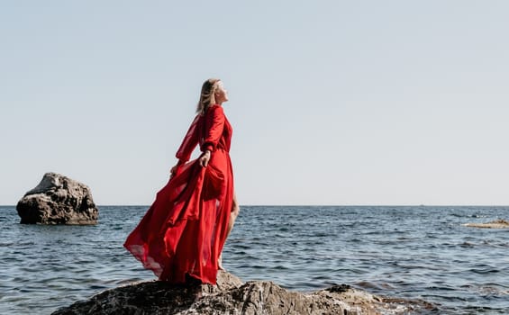 Woman travel sea. Young Happy woman in a long red dress posing on a beach near the sea on background of volcanic rocks, like in Iceland, sharing travel adventure journey