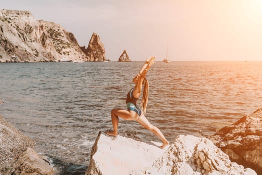 Yoga on the beach. A happy woman meditating in a yoga pose on the beach, surrounded by the ocean and rock mountains, promoting a healthy lifestyle outdoors in nature, and inspiring fitness concept