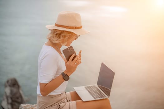 Freelance women sea working on the computer. Good looking middle aged woman typing on a laptop keyboard outdoors with a beautiful sea view. The concept of remote work