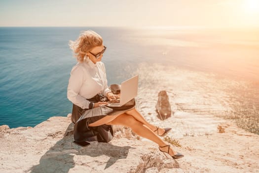 Business woman on nature in white shirt and black skirt. She works with an iPad in the open air with a beautiful view of the sea. The concept of remote work