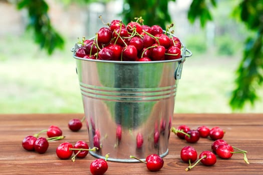 Fresh red ripe cherry in a bucket on the wooden background. Ripe red cherries in the metal bucket on a wooden background.