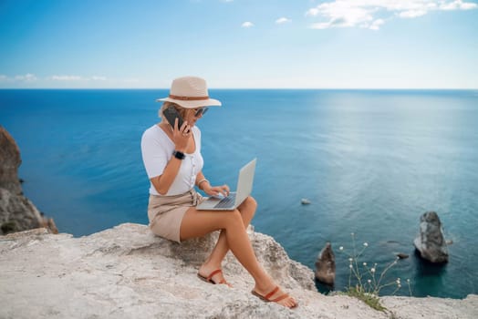 Freelance women sea working on the computer. Good looking middle aged woman typing on a laptop keyboard outdoors with a beautiful sea view. The concept of remote work