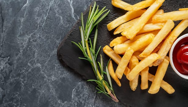 Crispy roasted chips from fresh potatoes on a dark marble surface with sea salt grains and French fries spice - Delicious fast food fried golden yellow