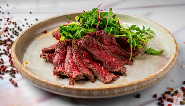 Beef sliced. macro photo of sliced __beef garnished with greens in a plate on a white marble serving tabl