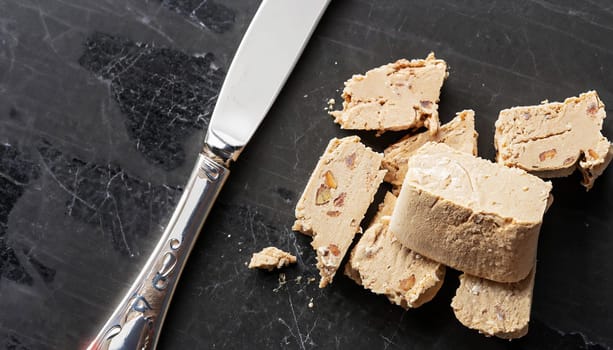 Sweet halva dessert slices with almonds and knife on old kitchen table. Top view.