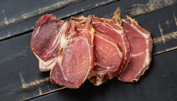 Dried lamb jerky slices on wooden board with salt and pepper