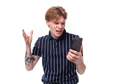 European young blond man in a T-shirt looks in disbelief at the phone screen on a white background.