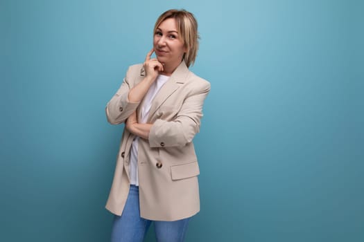 well-groomed blonde millennial woman in a beige jacket posing confidently on a blue background.