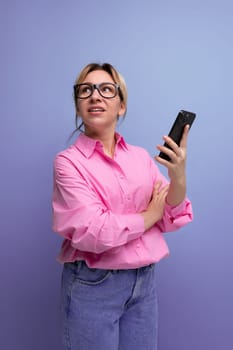 young confident blond woman with ponytail and glasses dressed in a fashionable pink shirt for the office solves work issues on the phone.