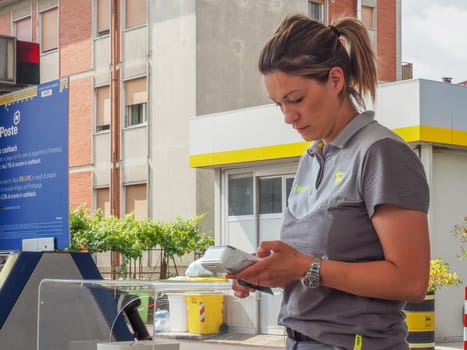 Cremona, Italy - July 3 2023 gas station attendant woman taking payments with credit card from customers outdoors near fuel pumps