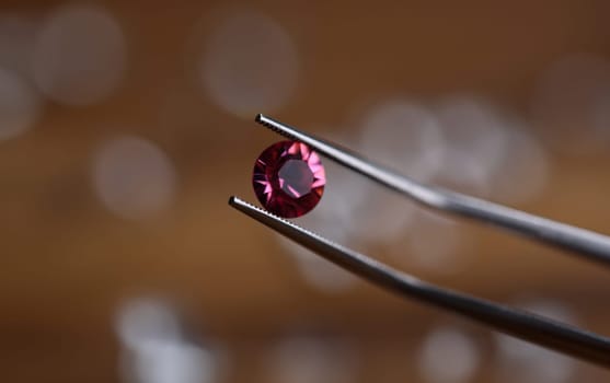 Close-up of tweezers holding gemstone. Professional jeweler using special equipment. Jeweller checking precious stone for identity. Jewelry production concept