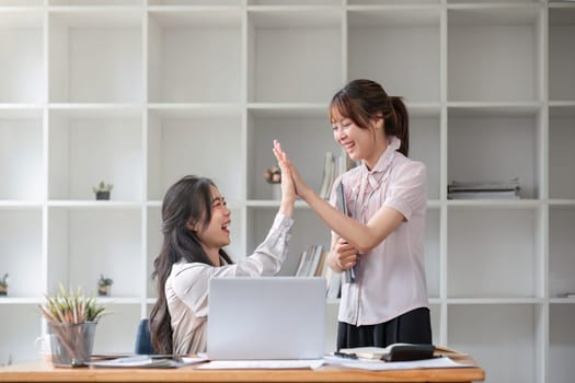 Two young Asian businesswoman smiling happy giving high five at the office. Young Asian woman or intern who successfully completes her goals..