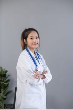 Young asian woman wearing doctor uniform standing with arms crossed gesture at clinic.