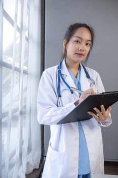 Portrait of female doctor wearing white coat with stethoscope holding clipboard and looking confidently to camera.