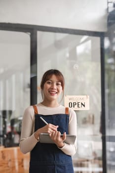 Successful small business owner. Beautiful girl with apron holding tablet standing in coffee shop restaurant. Portrait of asian woman barista cafe owner..