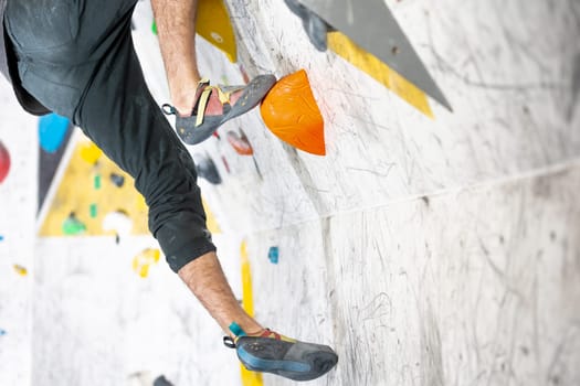 Young climber climbing on a boulder wall indoor, rear view, concept of extreme sports and bouldering