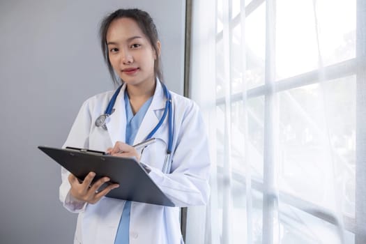 Portrait of female doctor wearing white coat with stethoscope holding clipboard and looking confidently to camera.