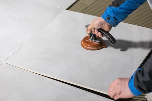 Tiler worker placing or tiling gray ceramic tile in position over adhesive glue with lash tile leveling system, renovation or recontruction, concept of building