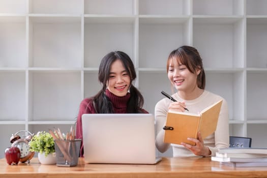 Two young female students tutoring and catching up workbook together.