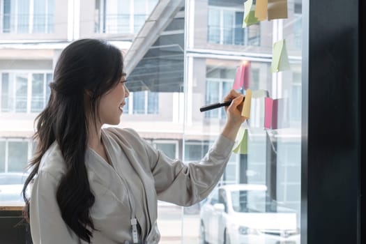 Close up hand businesswoman writing sticky notes on glass wall in office.