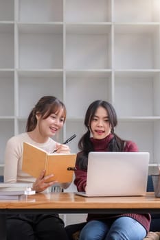 Two young female students tutoring and catching up workbook together.