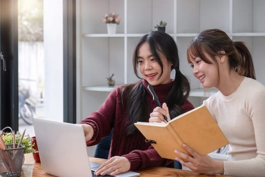 Two young female students tutoring and catching up workbook together.