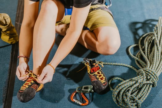 Young woman climber prepare before to climbing on a boulder wall indoor with equipment, shoe, rope, carabiner, concept of extreme sports and bouldering
