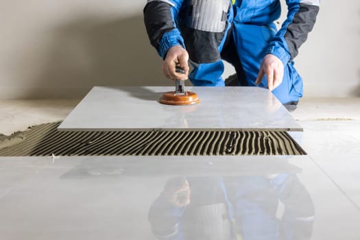 Tiler worker placing or tiling gray ceramic tile in position over adhesive glue with lash tile leveling system, renovation or recontruction, concept of building