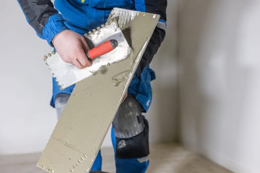 Tiler worker placing or tiling gray ceramic tile in position over adhesive glue with lash tile leveling system, renovation or recontruction, concept of building