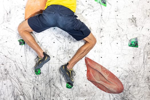 Close up view of young man or climber feet in climbing shoes on artificial indoor wall at the climbing center, sport activity concept