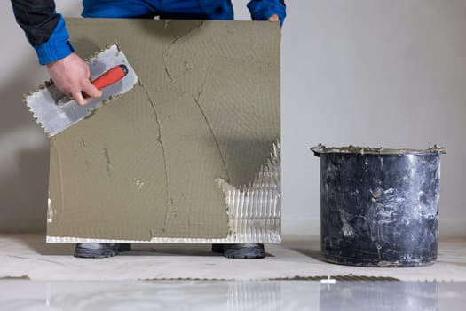 Tiler worker placing or tiling gray ceramic tile in position over adhesive glue with lash tile leveling system, renovation or recontruction, concept of building