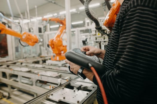 Technical engineer adjusting robotic arm in the industrial automotive hall, industry concept