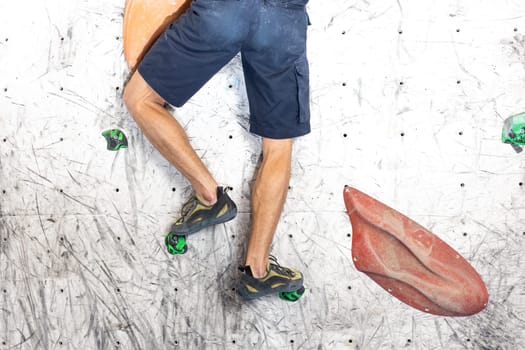 Close up view of young man or climber feet in climbing shoes on artificial indoor wall at the climbing center, sport activity concept