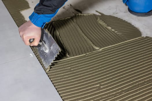 Tiler worker placing or tiling gray ceramic tile in position over adhesive glue with lash tile leveling system, renovation or recontruction, concept of building