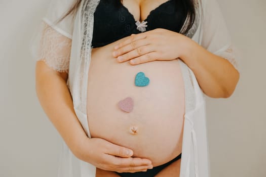 Young pregnant woman with belly and two heart stickers, pink and blue, a pregnancy concept