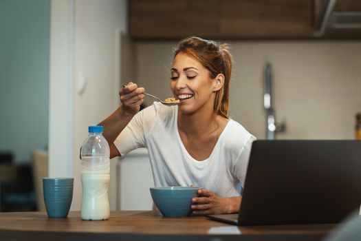 Beautiful young woman is eating her healthy breakfast in her kitchen.