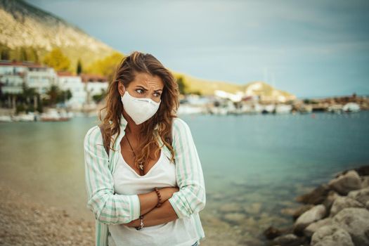 Shot of a concerned young woman with protective N95 mask at vacation on the seaside during the COVID-19.