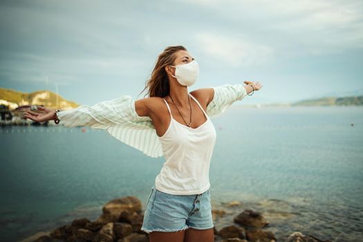 Shot of an attractive relaxed young woman with protective N95 mask enjoying a vacation on the beach during the COVID-19.