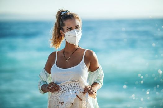 Shot of an attractive young woman with N95 protective mask enjoying a vacation on the beach during the COVID-19. She is self-isolation in nature.