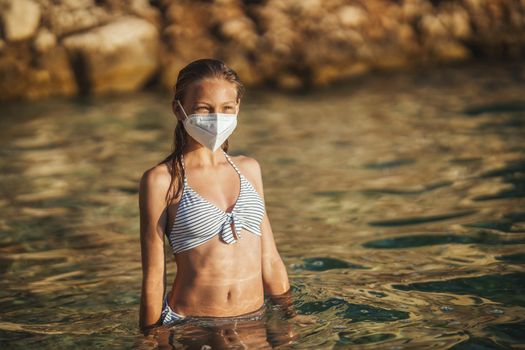 Shot of an happy teenager wearing surgical mask enjoying a vacation on the beach during the COVID-19.