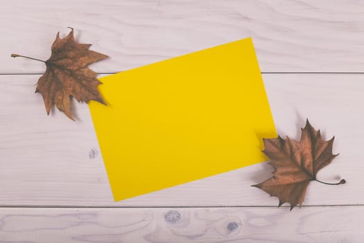 Empty yellow paper on wooden table with autumn leaves.Image is intentionally toned