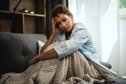 A unhappy young woman is sitting on the sofa at home. She is sad because the boyfriend  left her.