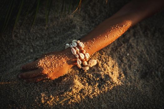 Close-up of a womans hand with shell bracelat at the sandy beach. Boho style.