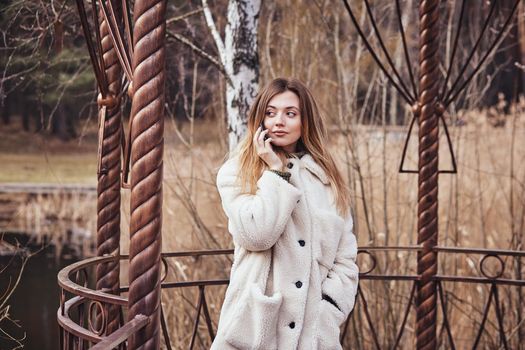 Happy beautiful young woman talking on mobile phone in the gazebo on the background of the pond