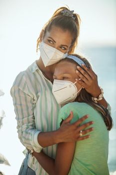 Shot of a smiling embraced sisters with protective N95 mask spending time on the seaside at corona pandemic. They are having self-isolation in nature.