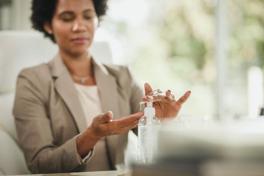 Cropped shot of an attractive African businesswoman sitting alone in her home office and using antiseptic gel to disinfect her hands during COVID-19 pandemic. Selective focus.