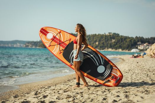 A young woman on a sea beach with a surfboard is ready for the waves.