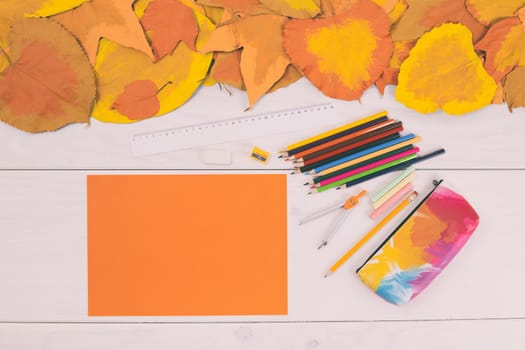 Empty orange paper and school supplies on wooden table with painted leaves.Toned image.